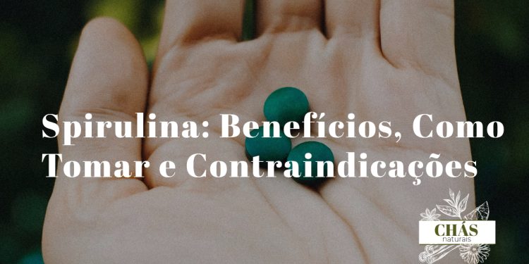 spirulina benefícios — pó de spirulina azul-esverdeado em colher com cápsulas