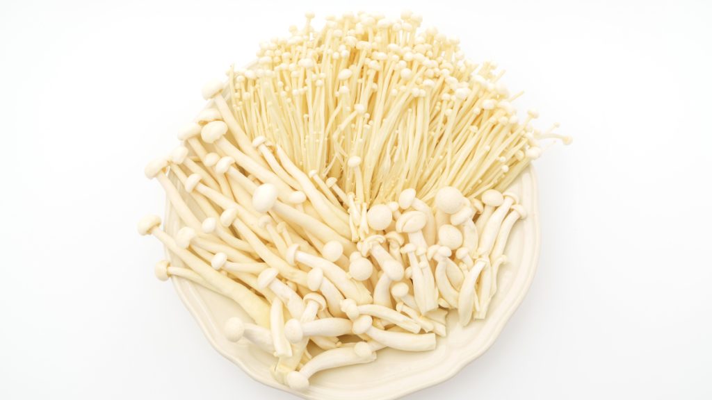 maço de enoki Flammulina velutipes frescos com cabos longos e cabeças brancas minúsculas sobre tábua de madeira japonesa com pauzinhos